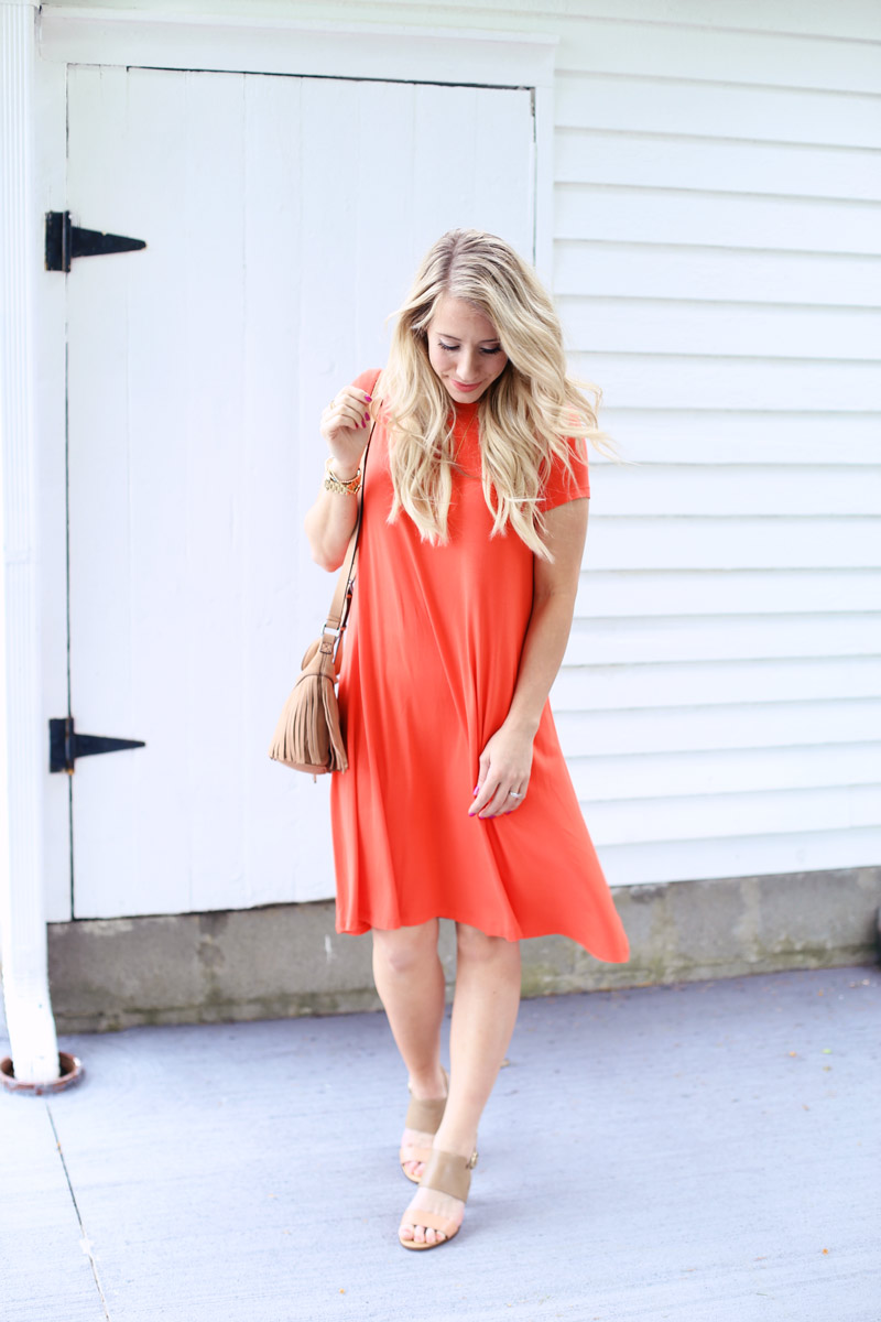 Wearing an orange coral dress and beige sandals, Abby looks at her feet.