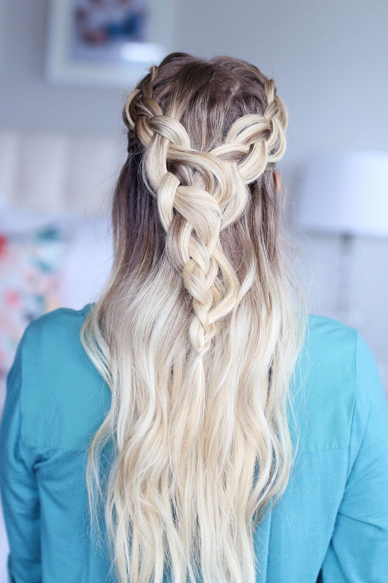 A close-up photo of a blonde woman facing away from the camera, her hair cascading down her back. Two braids come around each side of her head and meet at the back. Dutch braid hairstyles tutorial.