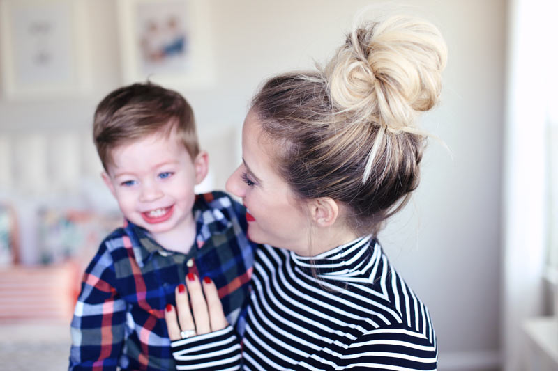 A mom with bright red lips and nails smiles proudly at her son. Twist Me Pretty.